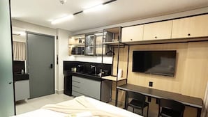 Quarto de hotel moderno com cama, escrivaninha, televisão e cozinha compacta.