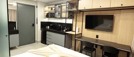 A modern hotel room with a bed, a desk, a TV, and a kitchenette.