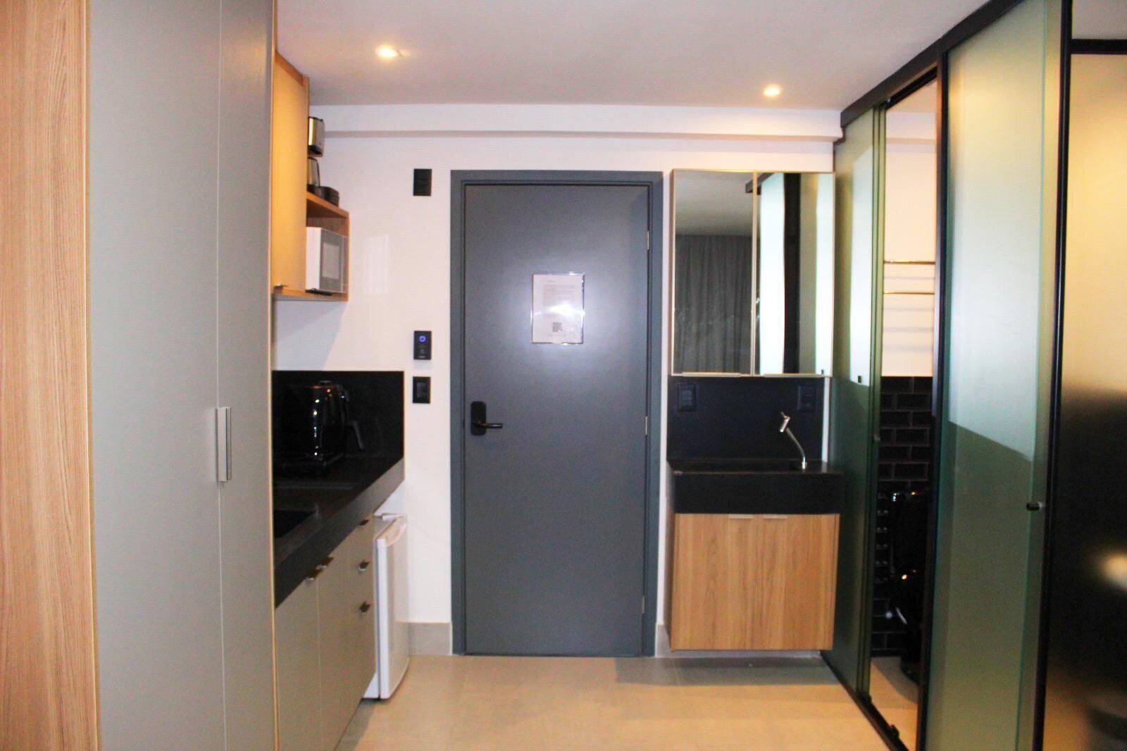 Cocina compacta con una puerta oscura, microondas, cafetera y lavabo con un mueble de madera.