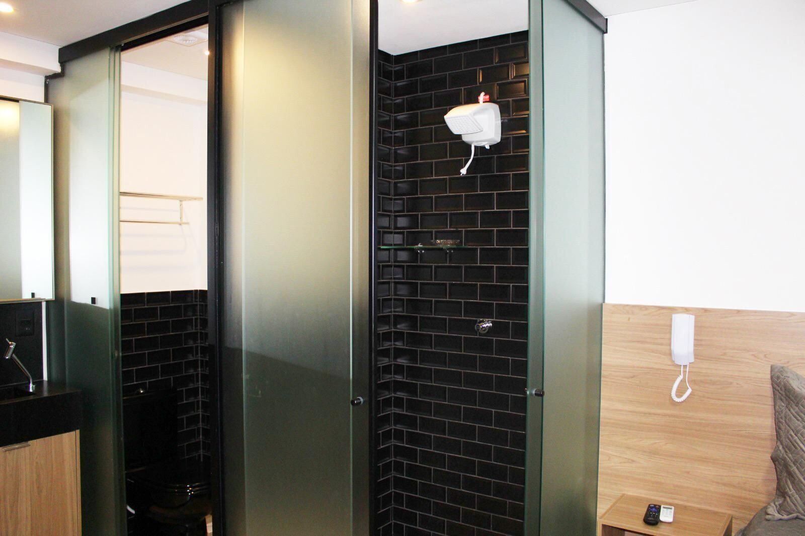 A modern bathroom with a black tiled shower, a glass partition, a wooden vanity, and a white telephone.