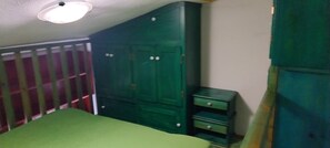 Una habitación con cama, un armario verde y una pequeña mesa.
