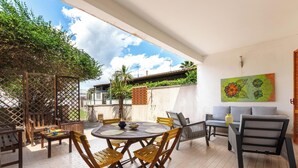 Un patio exterior con una mesa redonda y sillas, un sofá y un elemento decorativo en la pared.