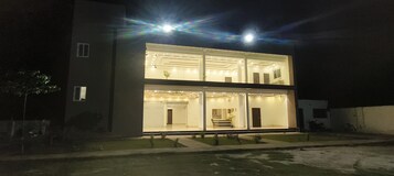 Un edificio moderno de dos pisos con fachada de vidrio, iluminación interior brillante y una escalera visible que conduce al nivel superior.