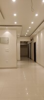 Un pasillo amplio y bien iluminado, con suelo de baldosas, luces empotradas en el techo y una puerta al final.