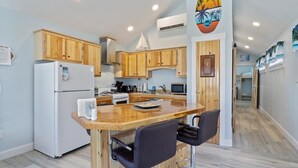 Een functionele keuken met houten kastjes, een witte koelkast, een magnetron en een klein eethoekje met twee stoelen.