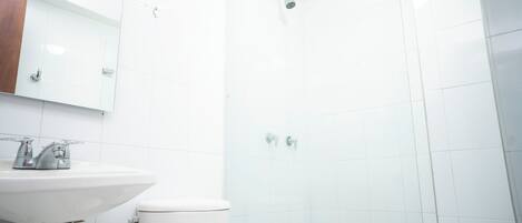Un baño con lavamanos blanco, inodoro y cabina de ducha de cristal.