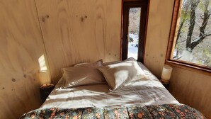 A cozy wooden room with a bed, a window, and a door. - El Arca Andina - Lonquimay (Lonquimay)
