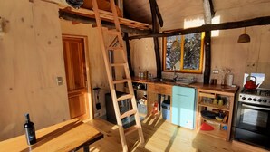 A cozy, rustic kitchen with wooden floors, a wooden bench, a ladder, a window with a view, and a stove. - El Arca Andina - Lonquimay (Lonquimay)