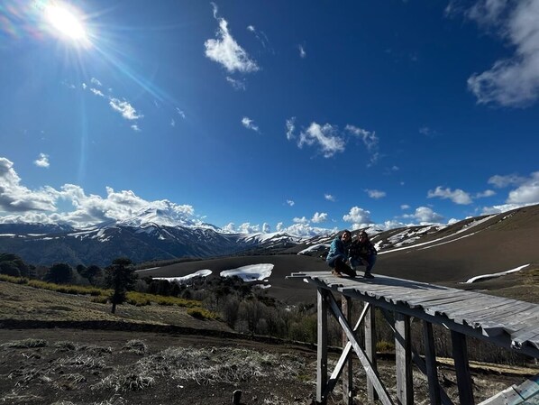 Une terrasse en bois surplombant un paysage montagneux, avec des zones enneigées et un ciel dégagé.