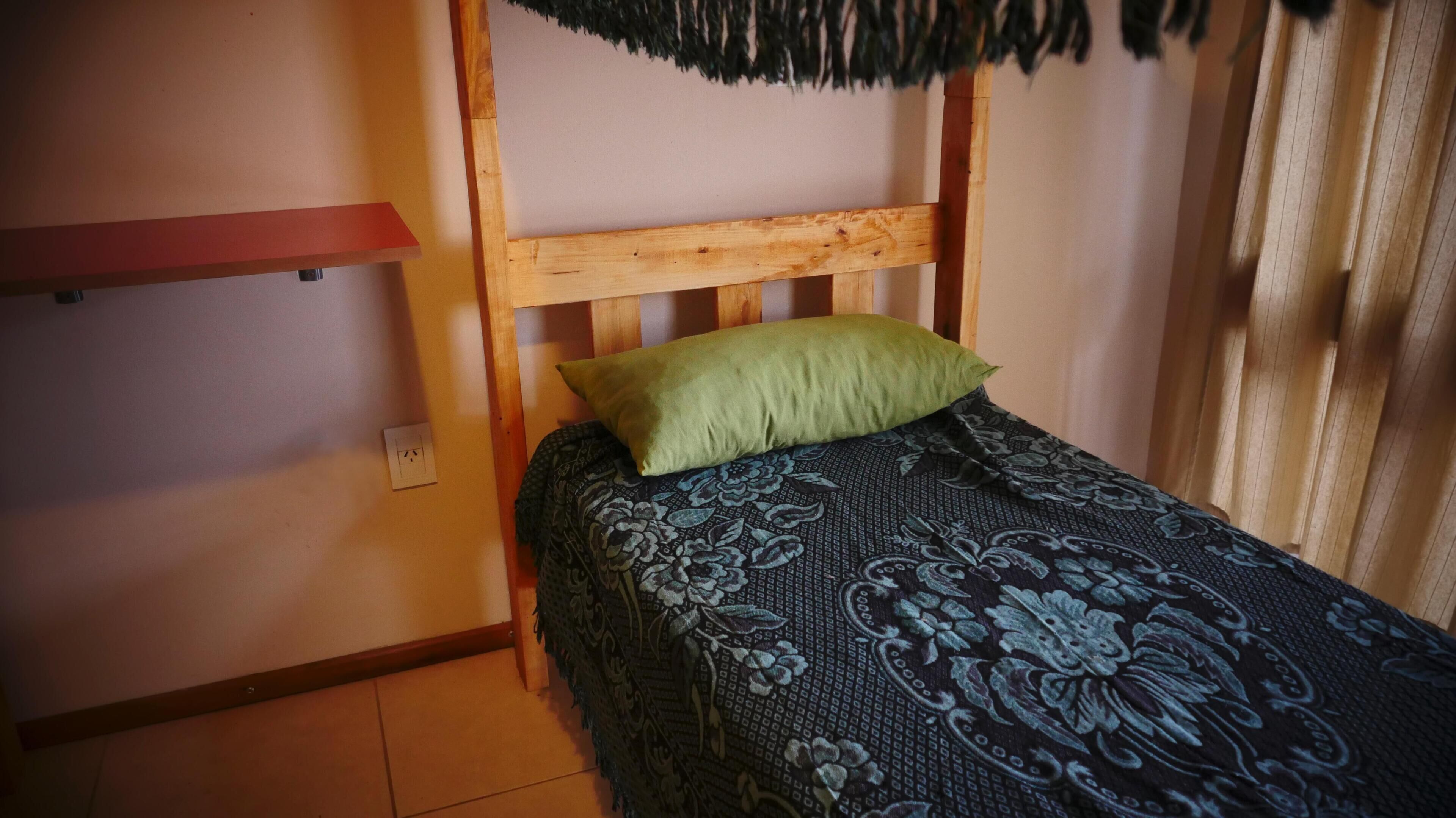 A single bed with a wooden headboard, a green pillow, and a floral-patterned bedspread.