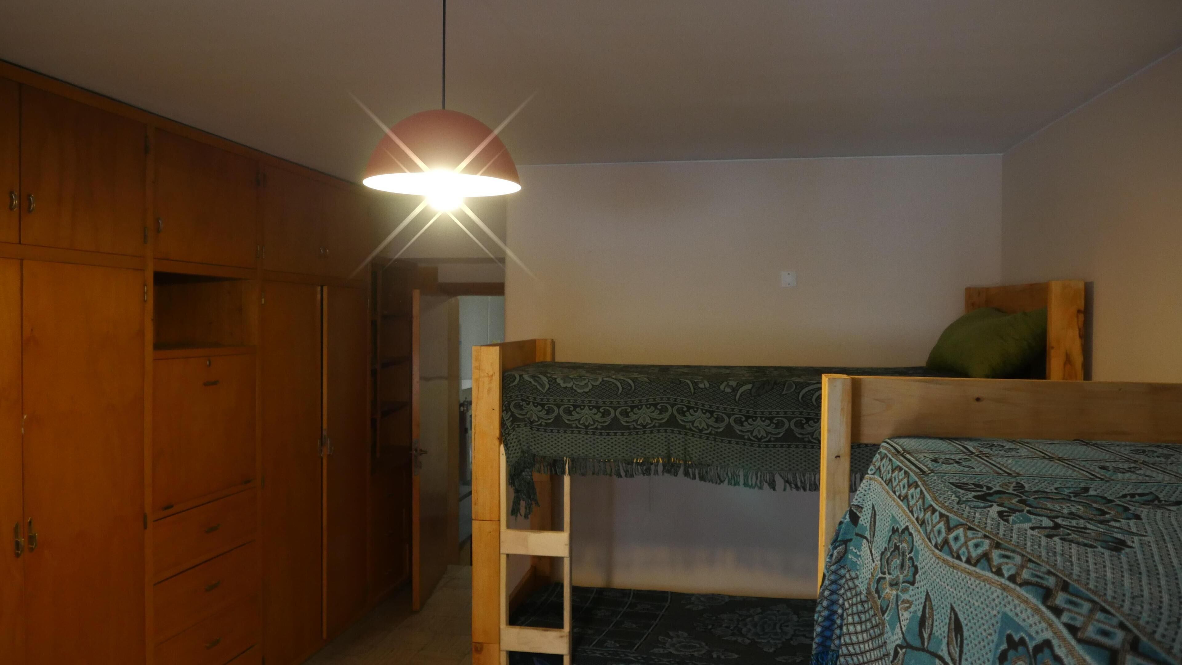 Et lille, svagt oplyst rum med køjeseng, træskab og en hængende lampe.