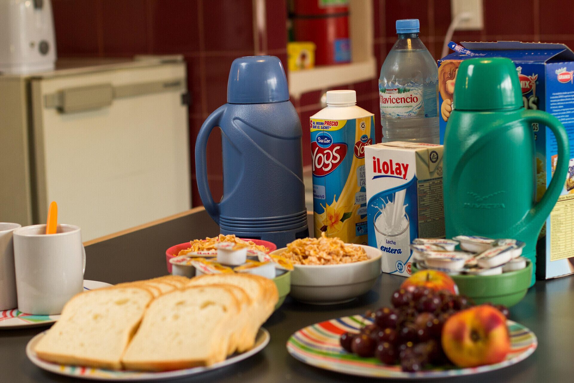 A breakfast table with cereal, milk, juice, and fruits.
