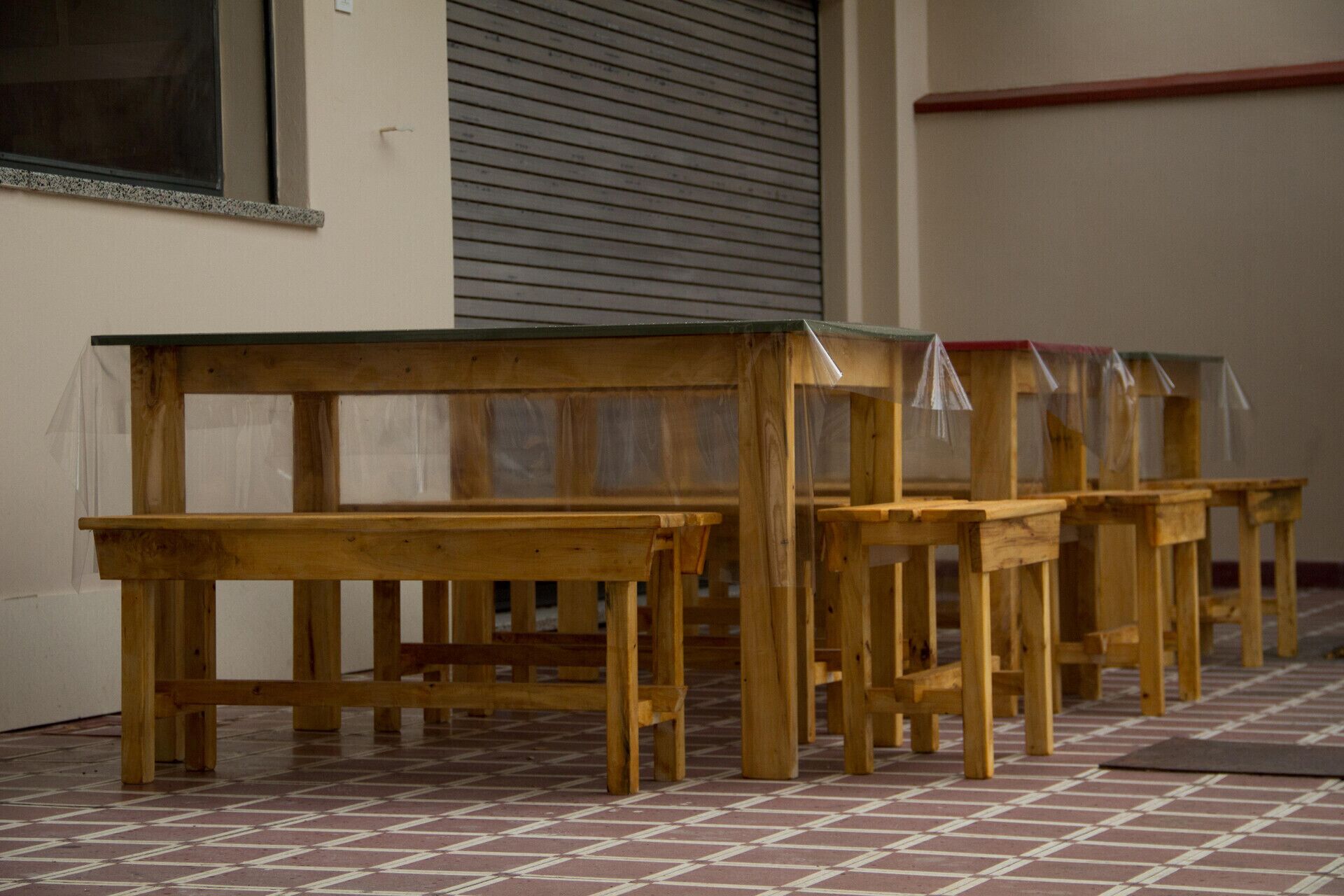 A row of wooden benches with transparent plastic covers, positioned outside a building with a tiled floor.