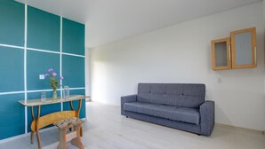 A room with a grey sofa, a wooden bench, a small table with a vase of flowers, and a teal accent wall. - Chastnyy Sektor (Bosteri)