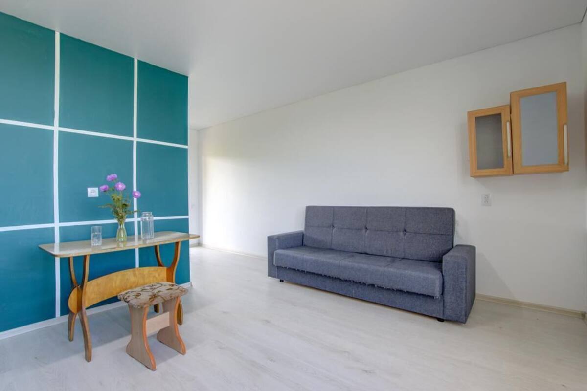 A room with a grey sofa, a wooden bench, a small table with a vase of flowers, and a teal accent wall.