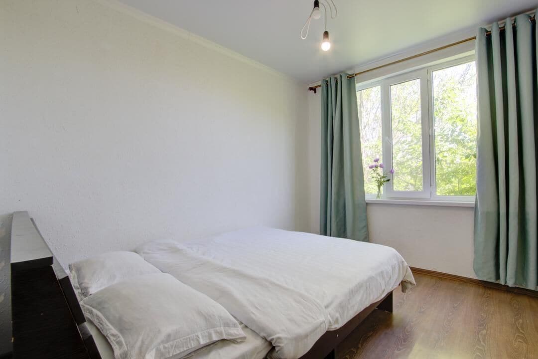 Een slaapkamer met een bed, een raam met gordijnen en een houten vloer.