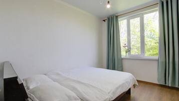 Een slaapkamer met een bed, een raam met gordijnen en een houten vloer.