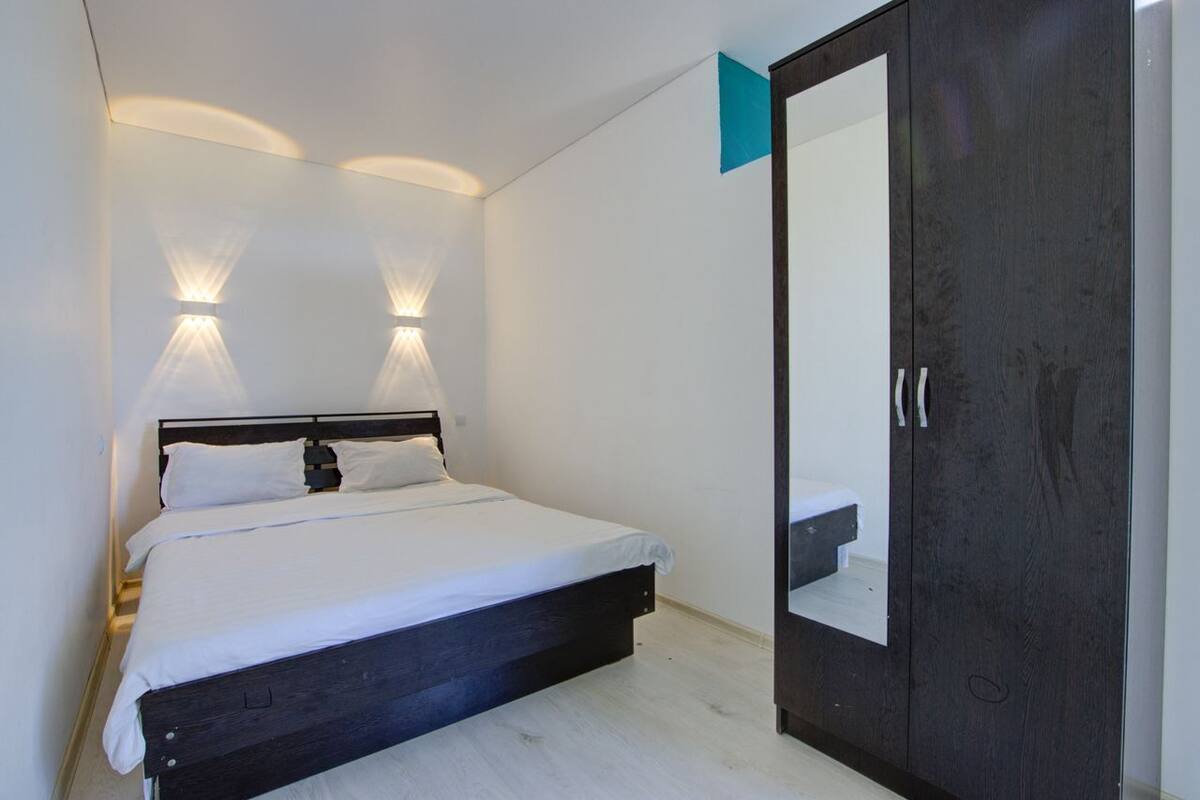 A bedroom with a bed, bedside lamps, a wardrobe, and a mirror.