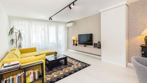 Ett modernt vardagsrum med en gul soffa, ett soffbord med böcker, en tv och en mönstrad matta.