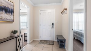 A hallway with a white door, a small bench, a potted plant, and a framed picture on the wall.
