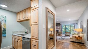 A modern kitchen with wooden cabinets and a built-in dishwasher, leading to a living area with a fireplace and large windows. - Camp Warnecke B111- Waters Edge - Stunning Remodel (New Braunfels)