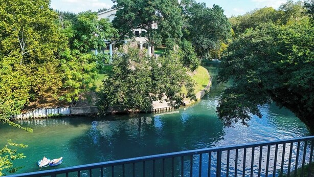 A river with a bridge, surrounded by trees and a building. - Camp Warnecke B111- Waters Edge - Stunning Remodel (New Braunfels)
