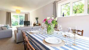 A dining area with a striped tablecloth, a vase of flowers, and wine glasses. - Pebble Place (Littlehampton)