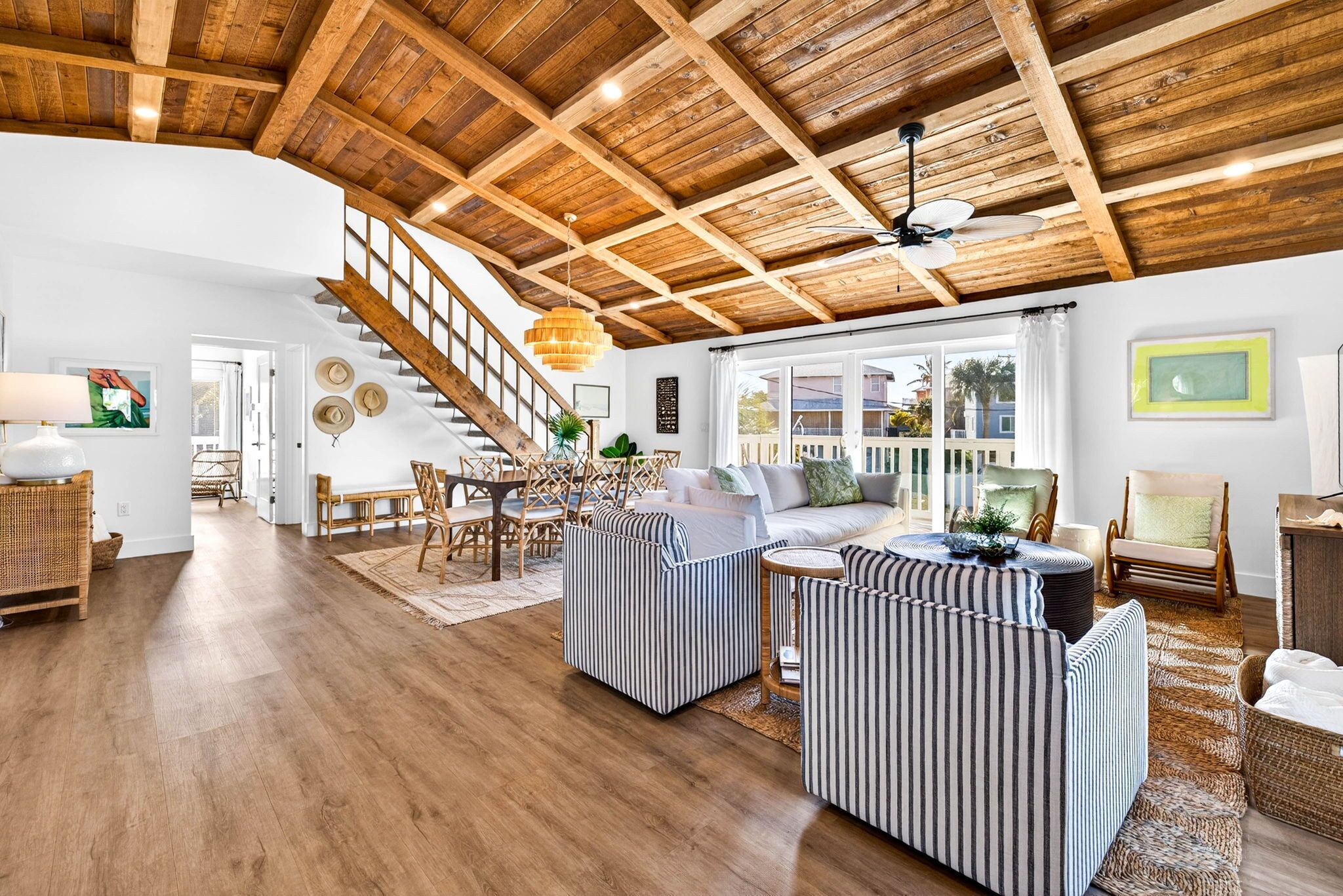 A spacious living room with a wooden ceiling, a staircase, and a large window.