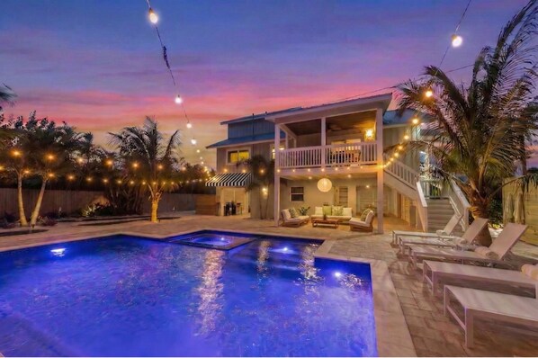 Una casa su due piani con piscina, area salotto esterna e luci decorative.