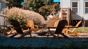 Un patio de grava con cuatro sillas Adirondack de madera dispuestas alrededor de un brasero.