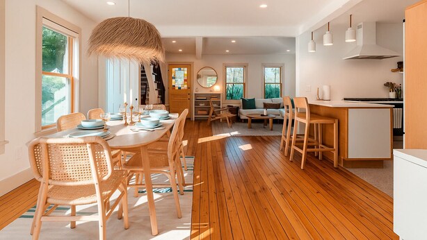 Una cocina moderna con suelo de madera, una zona de comedor con sillas de mimbre y un ventanal que proporciona luz natural.