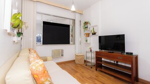 Sala de estar con sofá, televisor sobre un mueble de madera, radiador y ventana con cortinas.