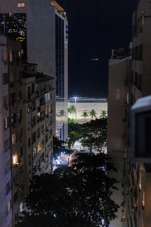 A nighttime view of a cityscape with tall buildings, a beach, and palm trees.