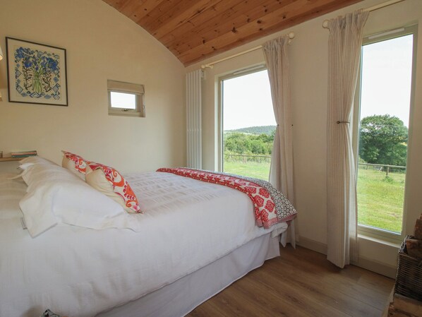 A bedroom with a large bed, a window with curtains, a small window, and a framed picture on the wall. - Owl's Hollow (Bucknell)