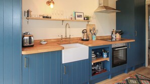 A kitchen with blue cabinets, a wooden countertop, a sink, a kettle, a toaster, and a stove. - Owl's Hollow (Bucknell)