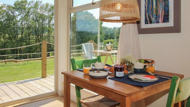 A dining area with a wooden table, chairs, and a hanging light fixture. A large window provides a view of the outdoors. - Owl's Hollow (Bucknell)