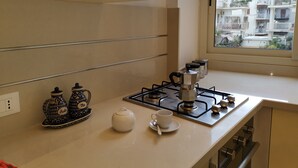 A kitchen with a gas stove, two teapots, a coffee pot, and a window with a view of a residential area. - If you feel like (Palermo)