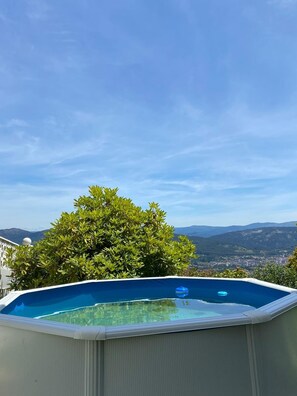 An outdoor swimming pool with a clear view of mountains and a tree in the background.