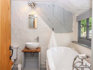 A bathroom with a white bathtub, a wooden vanity with a white sink, a mirror, and a towel hanging on the wall.