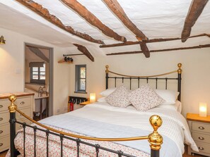 A bedroom with a bed, wooden beams, a window, a mirror, a dresser, and a nightstand.