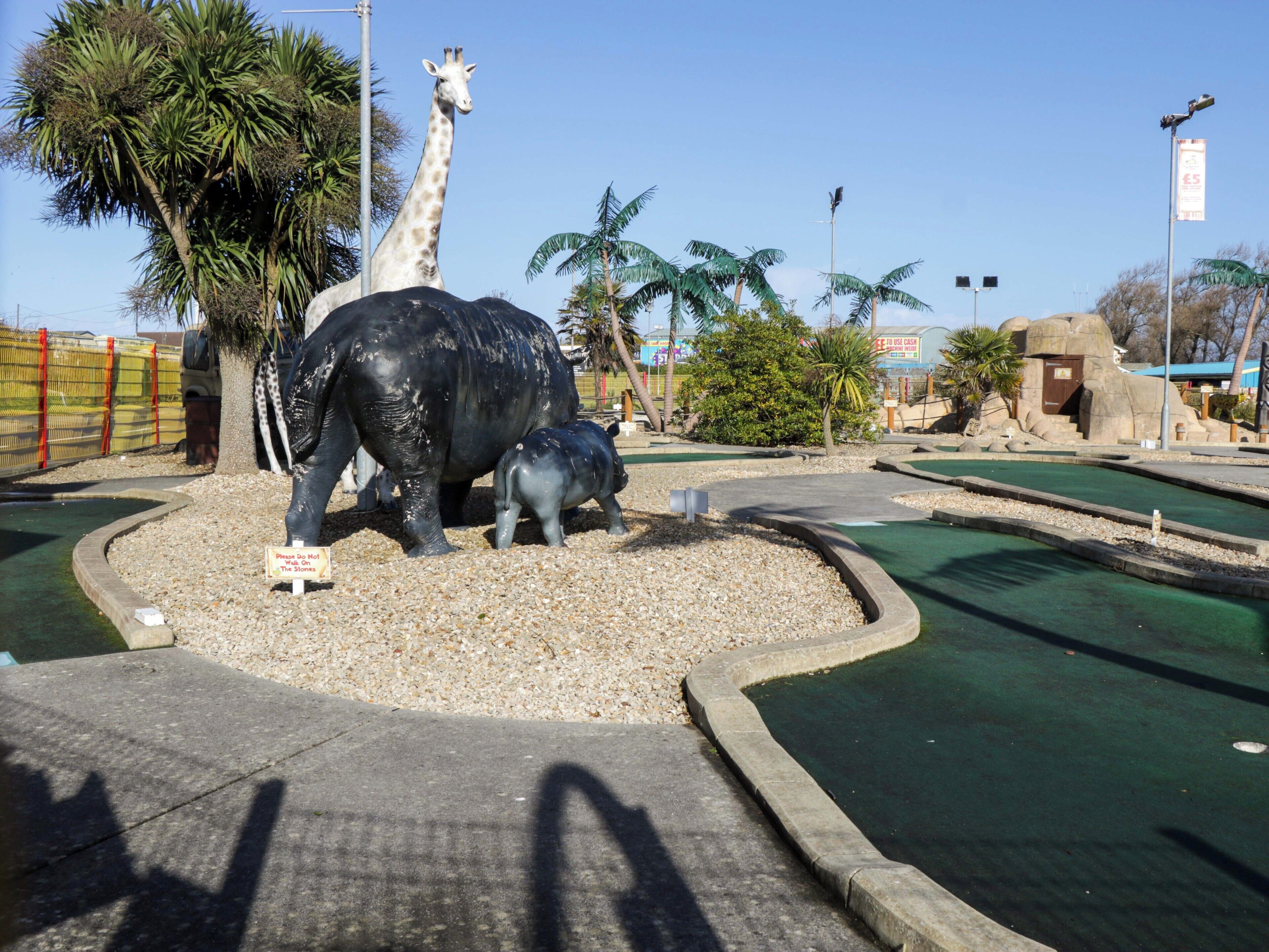 A zoo enclosure with a giraffe and a large elephant statue.