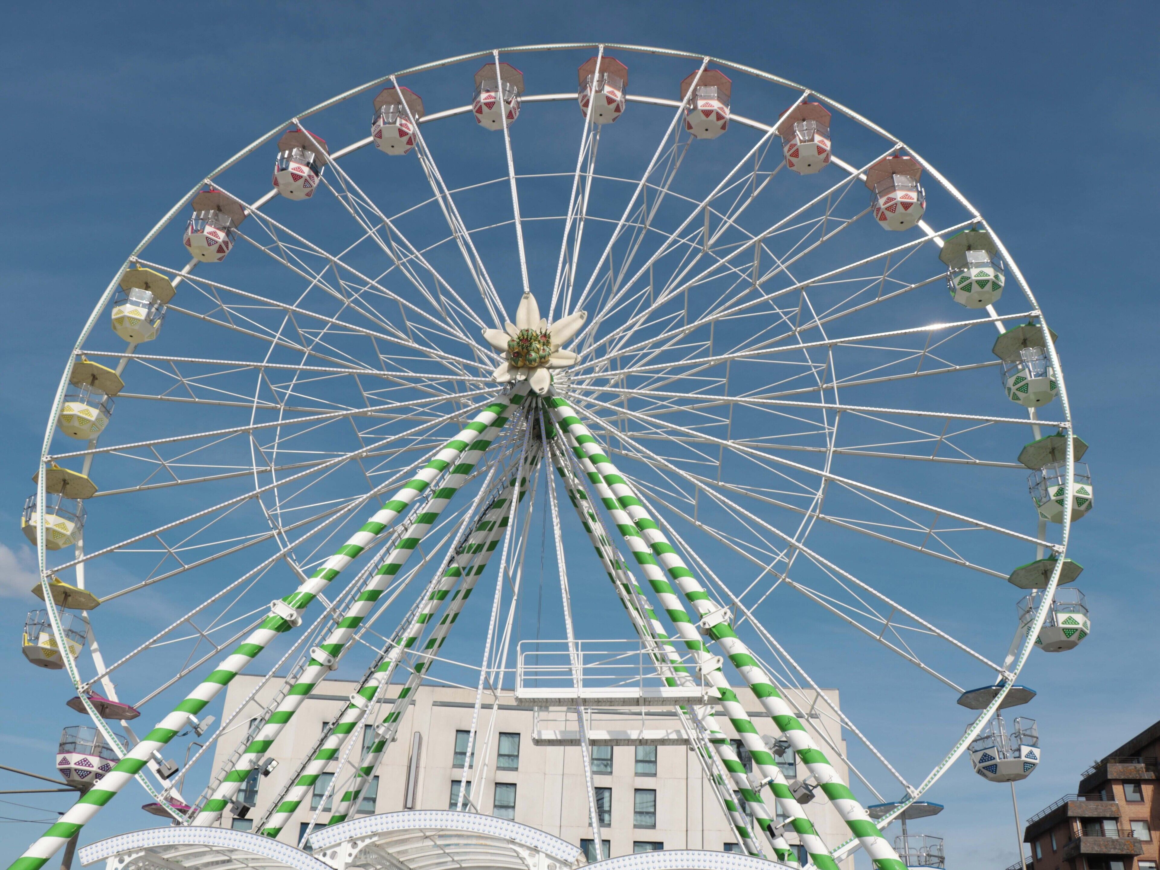A large Ferris wheel with green and white striped support beams, multiple cabins, and a building in the background.