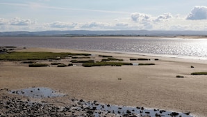 Een kustlandschap met een zandstrand, grasvelden en een rustige zee onder een licht bewolkte lucht.