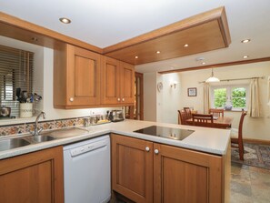 Una cocina con armarios de madera, lavavajillas y comedor con mesa y sillas.