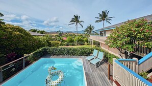 Uma área de piscina com deck de madeira, espreguiçadeiras e um flutuador.