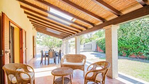 An outdoor patio with wicker furniture, a tiled floor, and a wooden pergola. - Is Carcuris 1P by All4sardinia  (Cardedu)