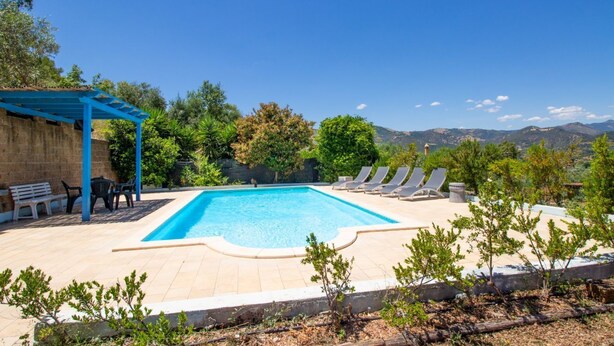 A swimming pool with lounge chairs and a pergola, surrounded by trees and mountains in the background. - Is Carcuris 1P by All4sardinia  (Cardedu)