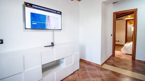 A modern living room with a flat-screen TV mounted on the wall, a white entertainment unit, and a tiled floor. - Is Carcuris 1P by All4sardinia  (Cardedu)