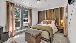 Een slaapkamer met een bed, nachtkastje, lamp, rieten mand en een raam met gordijnen.