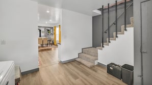 Een modern interieur met een trap, houten vloeren en een keuken in de achtergrond.